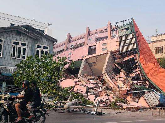 People ride on a motorbike past a destroyed building in Myanmar. 