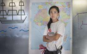An MSF humanitarian affairs officer stands in front of a map of Africa, looking into the camera confidently.
