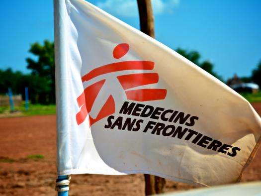 White flag with red logo of Doctors Without Borders/Médecins Sans Frontières (MSF) against sunny blue sky