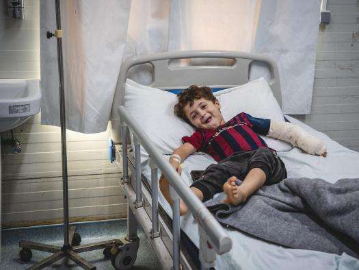 A smiling boy with an arm cast on a hospital bed in Mosul, Iraq.