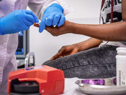 A close-up shot of an MSF doctor pricking a patient's finger to measure the glucose levels in their blood.
