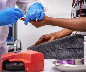 A close-up shot of an MSF doctor pricking a patient's finger to measure the glucose levels in their blood.