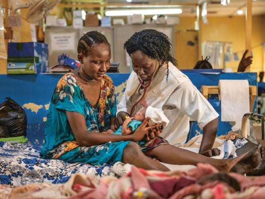 An MSF nurse and patient sit on a hospital bed with a newborn baby in Aweil, South Sudan.