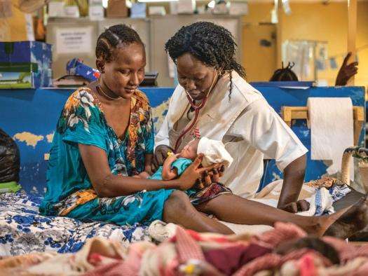 An MSF nurse and patient sit on a hospital bed with a newborn baby in Aweil, South Sudan.