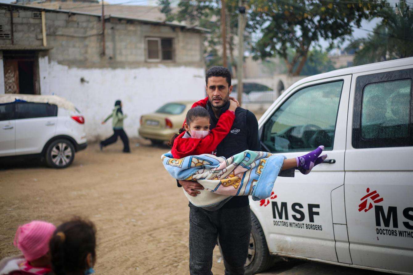A man carries a child to MSF's clinic at Rafah Indonesian Hospital in Gaza.