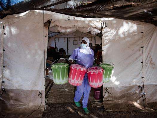 Cisse, a health promoter, carries buckets with kits given to every patient who comes to receive treatment for diphtheria from the logistics tent set up on the ground of the Centre de Traitement Epidemiologique in Guinea.