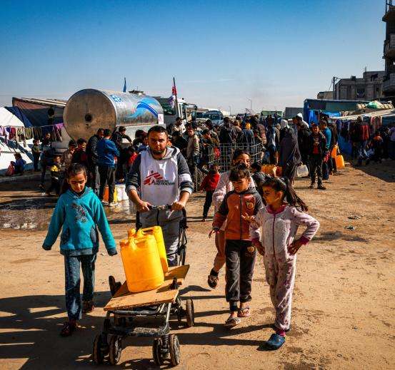 Youssef Al-Khishawi, an MSF water and sanitation agent, helps children carry water to their tent in the Tal Al-Sultan area of the southern Gaza town of Rafah, on January 27, 2024.