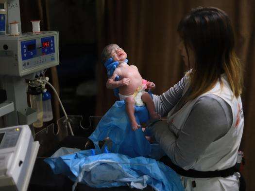 An MSF staff member in Gaza holds up a newborn baby at Nasser Hospital.