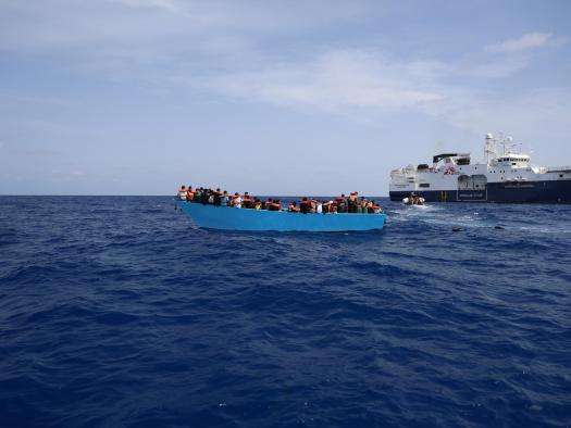 A search and rescue vessel approaches an overcrowded boat in the Mediterranean sea. 