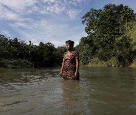 A woman stands in the middle of a river in Colombia.
