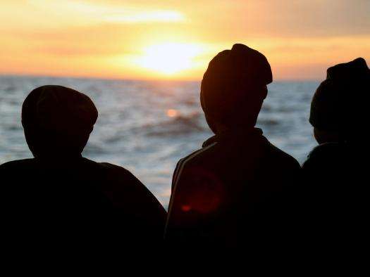 Survivors look over the deck of the Geo Barents at the sunset.