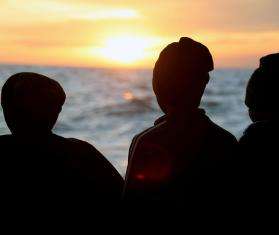 Survivors look over the deck of the Geo Barents at the sunset.