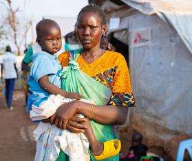 A woman stands in front of an MSF tent with her child in Juba, South Sudan.