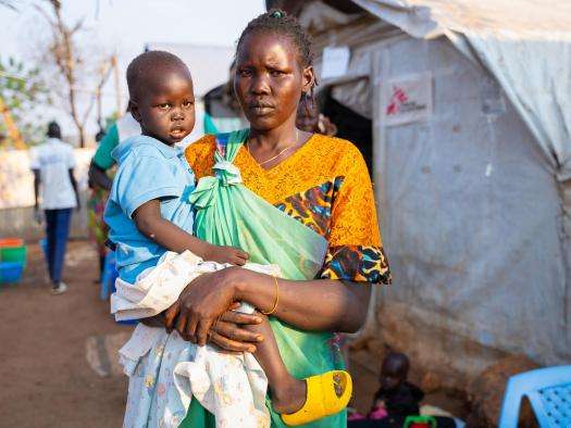 A woman stands in front of an MSF tent with her child in Juba, South Sudan.