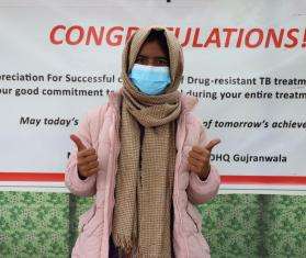 A woman in a face mask gives a thumbs up sign in Pakistan. 