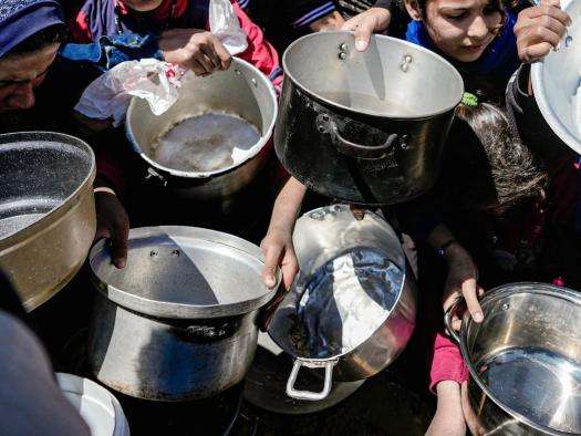 People hold empty pots waiting for a food distribution in Gaza. 