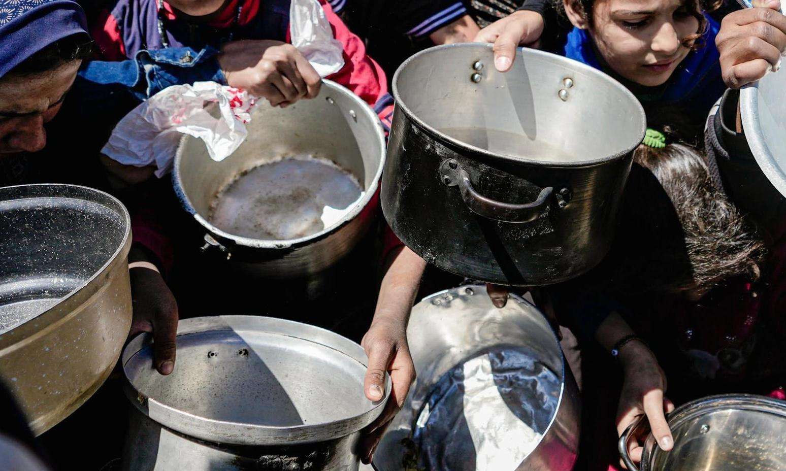 People hold empty pots waiting for a food distribution in Gaza. 