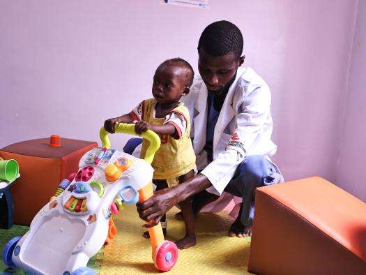 MSF physiotherapist Mubarak guides Usman, a 13-month-old child, walk with the aid of a plastic push-toy during a group session with tje caregivers of children suffering from malnutrition in Kano state, Nigeria