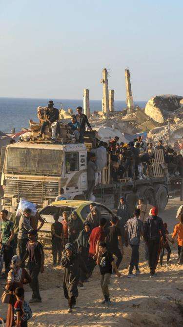 People line up next to trucks filled with armed guards to receive aid in Gaza. 