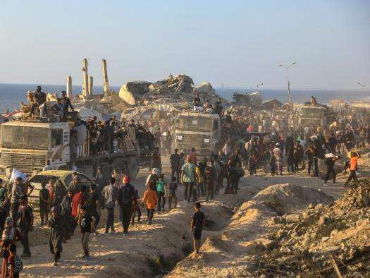 People line up next to trucks filled with armed guards to receive aid in Gaza. 