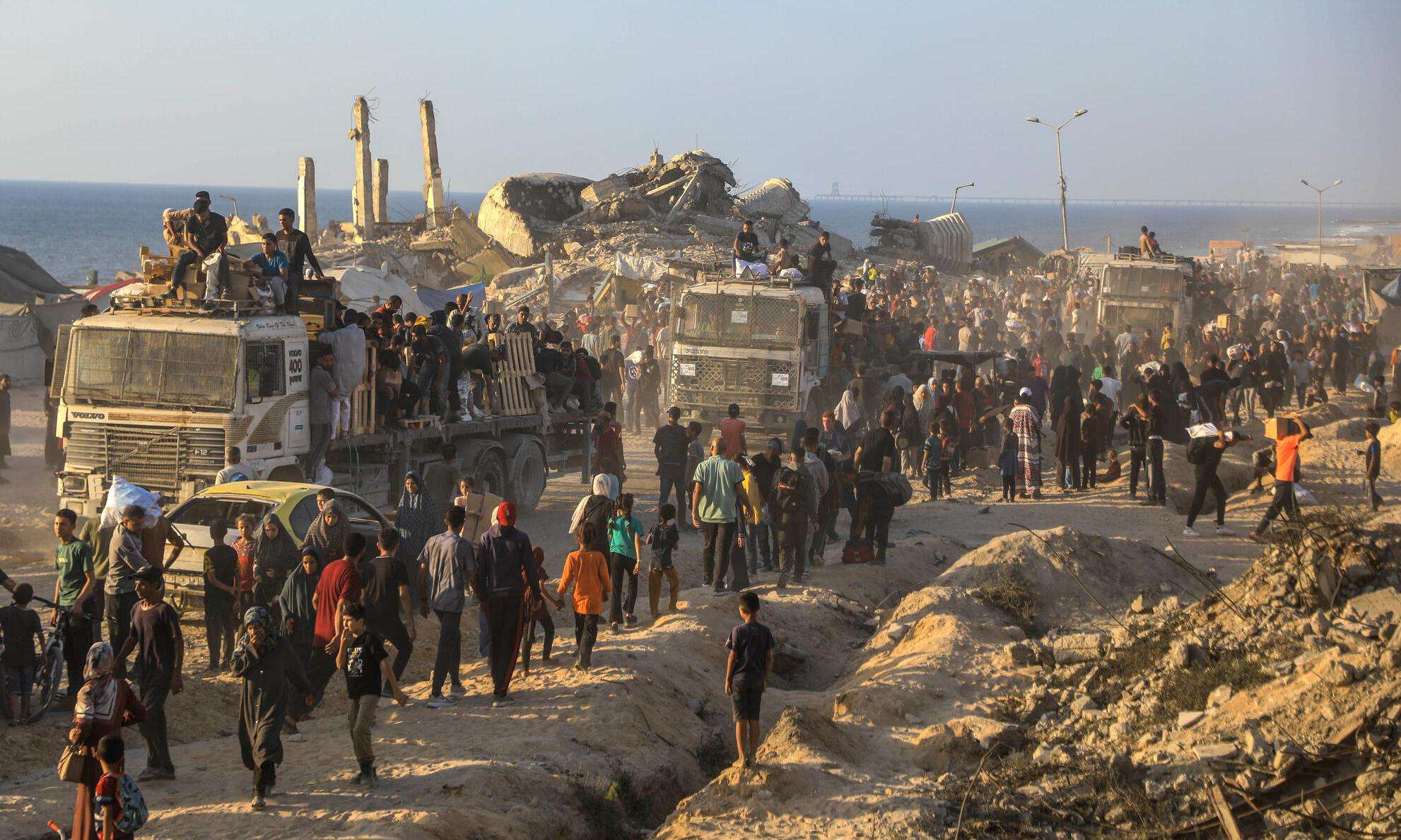 People line up next to trucks filled with armed guards to receive aid in Gaza. 