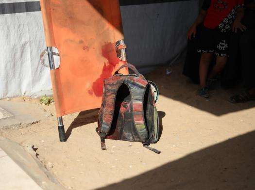 A backpack sits on the ground next to a bloody stretcher in Gaza, Palestine. 
