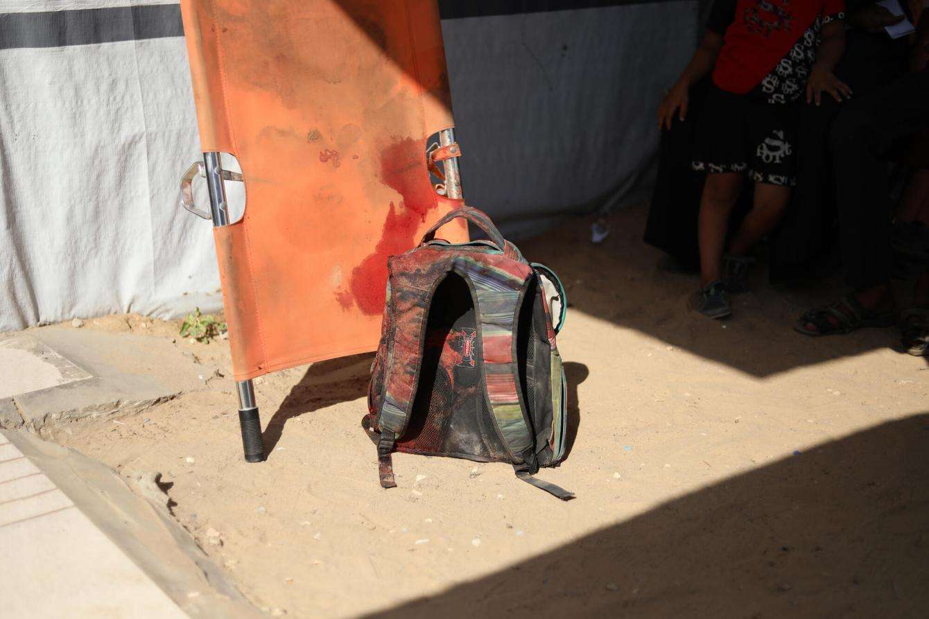 A backpack sits on the ground next to a bloody stretcher in Gaza, Palestine. 