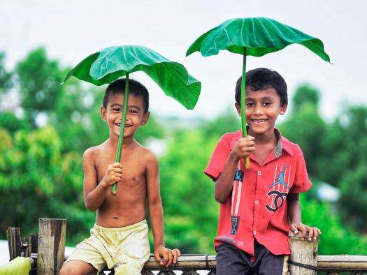 Two boys hold taro leaves above their heads in Bangladesh. 