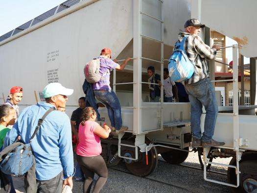 Men, women, and children board the moving train to reach the northern border of Mexico.
