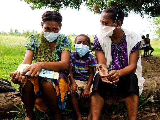 A child sits between two people in surgical masks after completing TB treatment from MSF in Papua New Guinea.