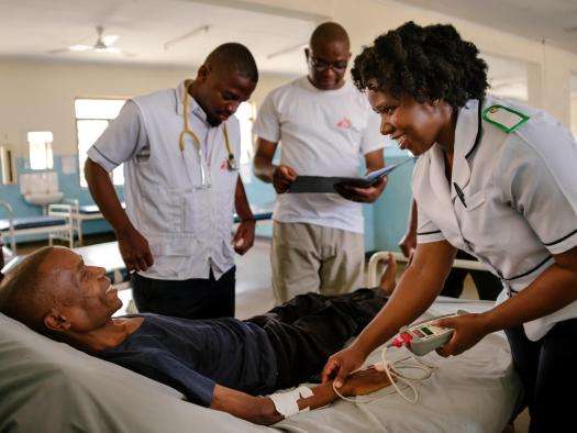 A group of MSF medics gathered around a patient in a hospital bed.